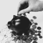 Ubezpieczenia inwestycyjne w Tarnowie - świnka skarbonka i dłoń wrzucająca do skarbonki monetę.